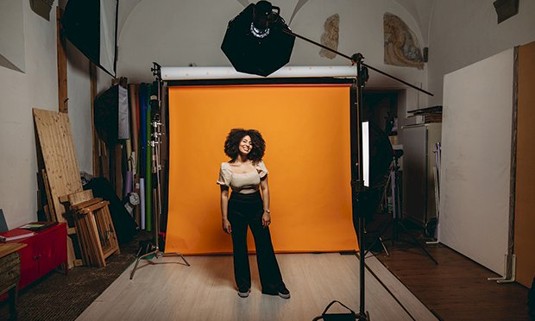 A lady stood on an orange background about to begin a photoshoot.