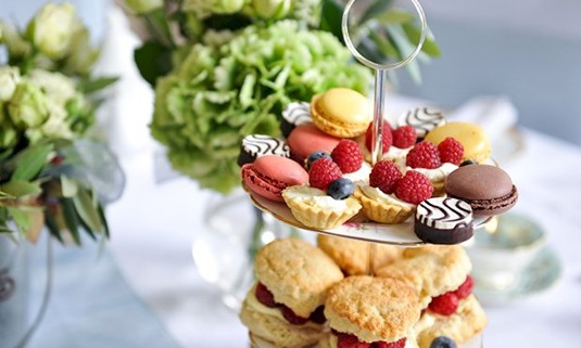 A table with ckaes and sandwiches and a glass of wine 