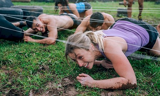 Two ladies crawling through a muddy assault course
