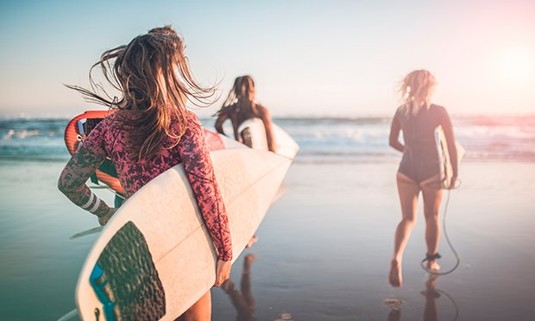 Three ladies with surf boards running towards to sea.