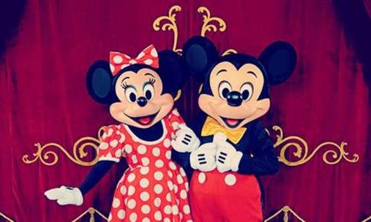 Minnie Mouse and Mickey Mouse with arms linked in front of a gold embellished curtain. Discover Disneyland Paris Hen Party ideas below: