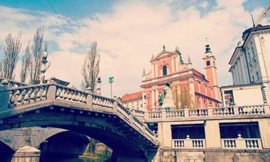 The orange hue of the Franciscan Church of the Annunciation in the background of a photo of the Triple Bridge over the Ljubljanica River. Explore Ljubljana Hen Party ideas below: