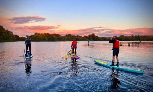 A group of friends paddleboarding at sunset on a hen do
