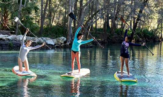 Three ladies on paddles boards on a lake doing yoga